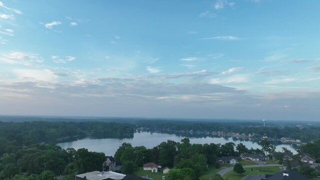 Aerial 4K of a calm lakeside community at early morning under semi-cloudy skies&mdash;glassy water, lush trees, and waterfront homes; perfect for travel, real estate, and lifestyle b-roll.