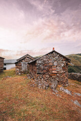 Obraz premium Rustic stone houses in the Asturian mountains of Spain, illuminated by warm sunset light under a colorful sky, representing traditional rural architecture on the Camino de Santiago; wide-angle view