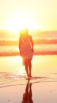 Attractive Asian woman enjoys a walk on the beach at sunset in Southern California. Slow Motion. Vertical Video.