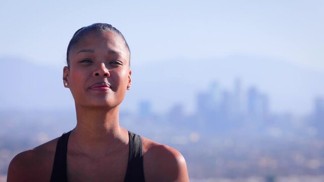 Mixed ethnicity (Asian-African) woman exercising in the park. The Los Angles skyline can be seen in the distance.