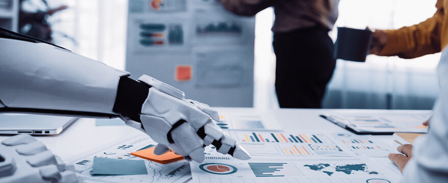 A robotic hand interacts with business reports in a modern office, showcasing collaboration and innovation. Colleagues discuss strategies while analyzing data.Noogenesis - Powered by Adobe