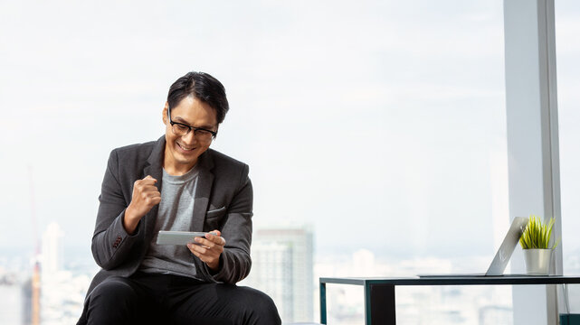 Young businessman using smartphone to play games to relax from work, using smartphone to trade stocks, showing happy expression, smiling face, Coppy space for text, banner.