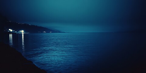 Nighttime coastal scene with hazy, dark blue water and illuminated shoreline