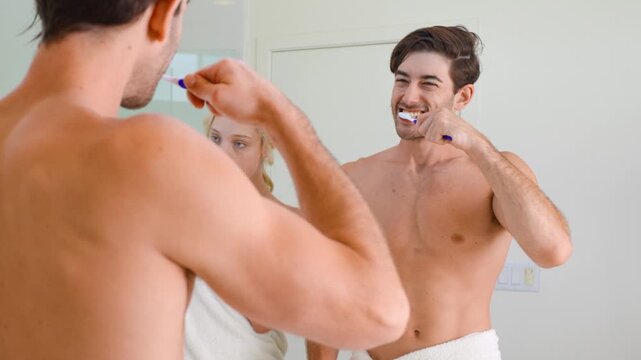 Fit man brushing his teeth while looking into the bathroom mirror.
