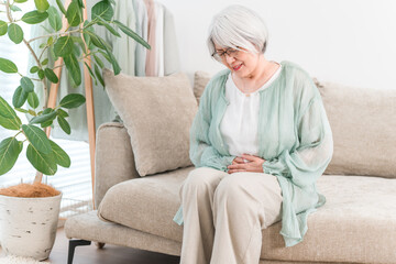 A senior woman with gray and silver hair suffering from stomach pain
