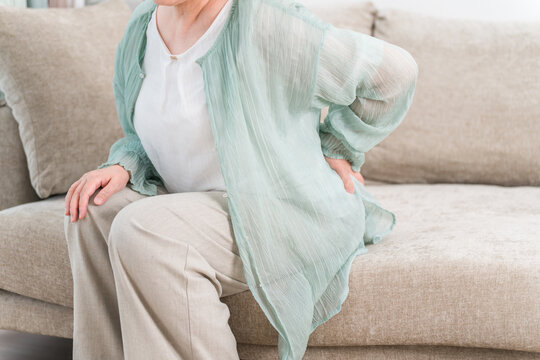Senior woman suffering from back pain on the living room sofa

