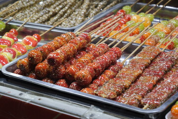 Close-up of various traditional Chinese tanghulu (sugar-coated fruit skewers) on display at a street food market.