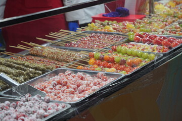 Close-up of various traditional Chinese tanghulu (sugar-coated fruit skewers) on display at a street food market.