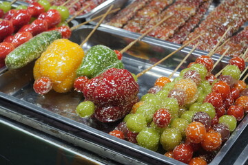 Close-up of various traditional Chinese tanghulu (sugar-coated fruit skewers) on display at a street food market.