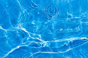 Blue water with ripples on the surface. Defocus blurred transparent blue colored clear calm water surface texture with splashes and bubbles. Water waves with shining pattern texture background.
