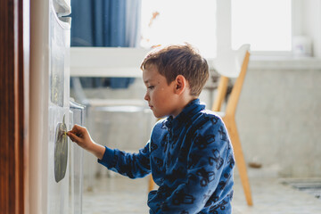 A young boy is focused on drawing on the refrigerator with a marker in a bright and inviting kitchen