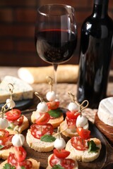 Delicious bruschettas with salami, mozzarella and tomatoes served with red wine on table, closeup