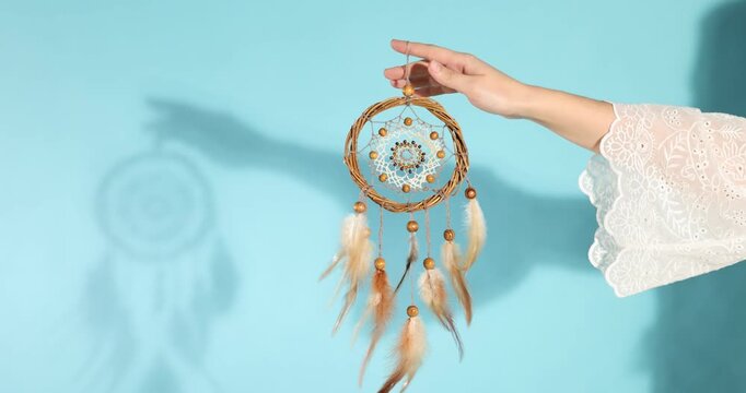 Woman with beautiful dream catcher on light blue background, closeup
