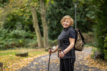 Senior woman enjoying a walk in a park during autumn with hiking poles and a backpack