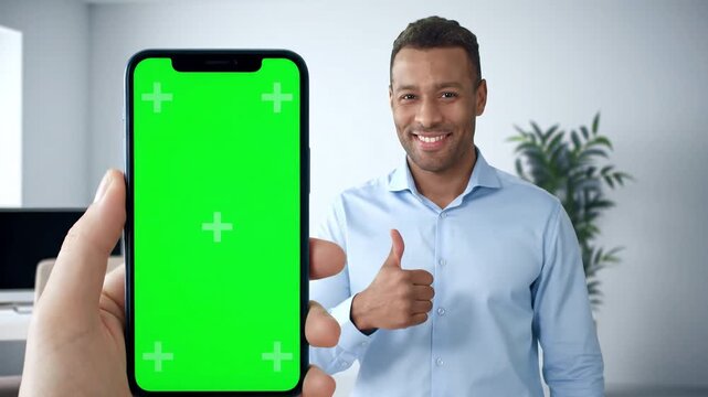 Happy Young Man Showing Thumbs Up While Person Holds Smartphone with Green Screen for App Promotion or Digital Content Display.