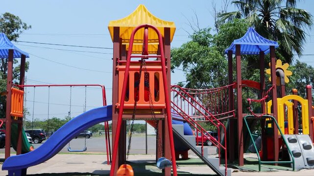 Upward camera movement showing colorful playground equipment and swings in a public park in Asuncion, Paraguay. Bright, playful outdoor recreation environment.