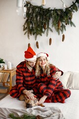 Couple wearing christmas plaid red pajamas with dog on bed