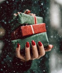 Woman's hand holding Christmas gift boxes in falling snow	