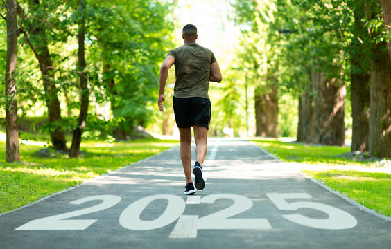 A man jogs along a tree-lined path in a vibrant park, with the year 2025 painted on the ground. The scene captures a sense of progress and health in an outdoor setting.