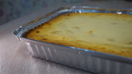 Freshly baked cottage cheese casserole in a foil tray, cooling on a table. Close-up homemade dessert shot suitable for recipe content, food blogs, and home cooking themes.