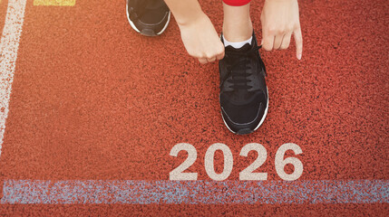 A collection of athletic shoes is placed on a bright red track, highlighting the year 2026. The setting captures the excitement of sports and competition, encouraging action.