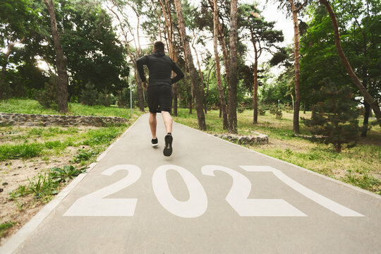 A man jogs down a peaceful forest path, with the numbers 2021 painted on the ground. This scene captures the essence of fitness and personal growth in a natural setting.