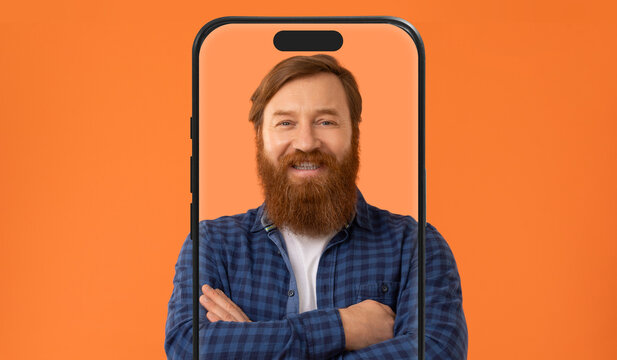 A man with a full beard stands confidently with his arms crossed, smiling warmly. He is framed by a large phone screen on a bright orange background, creating a modern and cheerful atmosphere.