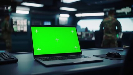 Laptop with Green Screen Mockup on a Desk in a Futuristic Control Room or Command Center with Blurry Background of Technicians and Monitors. - Powered by Adobe