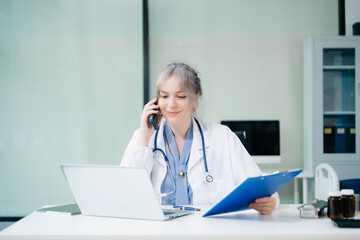 Beautiful physician doctor sit on table in office hospital. Attractive therapist female practitioner pharmacist smile and use tablet and laptop