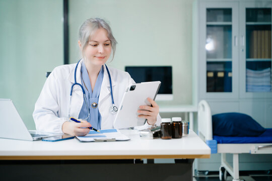 Smiling female doctor using smartphone while reviewing medical chart. Modern telemedicine, digital health records, and remote care concept. Real people in clinic. - Powered by Adobe