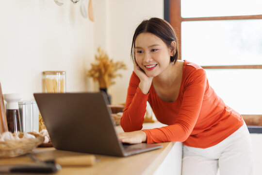 Asian woman in a kitchen using laptop at home
