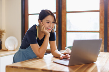 Interested woman look into laptop screen, choosing film, program, movie, video to watch while cooking in kitchen. asian female reading food recipes in internet, surfing in social networks, web pages
