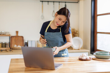 Woman, cooking in kitchen with laptop for live streaming, online recipe and meal prep by stove. Nutrition influencer, food blogger or vegan chef with social media tutorial in apartment
