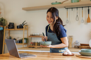 Woman, cooking in kitchen with laptop for live streaming, online recipe and meal prep by stove. Nutrition influencer, food blogger or vegan chef with social media tutorial in apartment