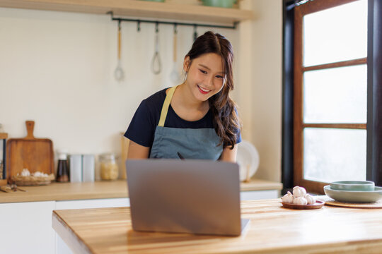 Woman, cooking in kitchen with laptop for live streaming, online recipe and meal prep by stove. Nutrition influencer, food blogger or vegan chef with social media tutorial in apartment
 - Powered by Adobe