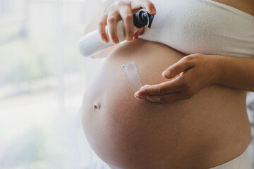 A pregnant woman applies skincare cream to her skin. This moment emphasizes self-care during pregnancy.