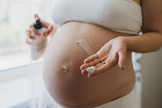 A pregnant woman applies skincare cream to her skin. This moment emphasizes self-care during pregnancy. - Powered by Adobe