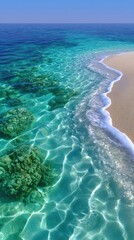 Obraz premium Vibrant turquoise ocean water laps gently onto a sun-drenched sandy beach revealing colorful coral reef formations beneath the crystal clear surface illuminated by bright daylight.