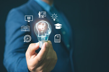 Businessman holding light bulb with human head icon and education symbols representing knowledge innovation, learning, e-learning, creativity, idea development, and business training concept.