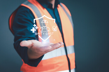 Engineer holding digital safety first icon with helmet and shield symbol representing construction safety, industrial protection, occupational health, and workplace safety management concept.