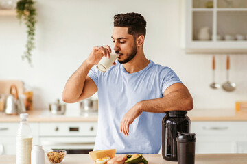 A young man sits at a kitchen counter drinking a glass of milk. Various healthy foods and protein...