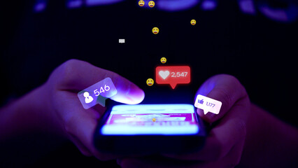 Close-up of hands holding a smartphone, scrolling social media with glowing icons for likes,...