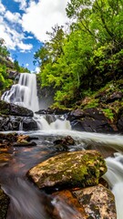 Cascading waterfall plunges among lush greenery and dark rocks under a cloudy sky