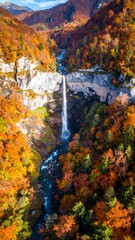 Cascading waterfall surrounded by autumn foliage and rocky cliffs from an aerial perspective