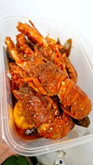 Cooked lobsters covered in a spicy red chili sauce in a plastic container.