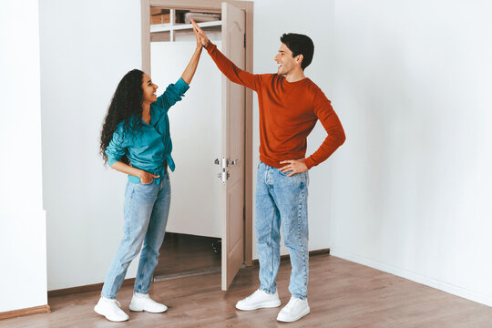 A couple is seen smiling and giving each other a high five in an empty room. They are dressed casually, and it appears they are enjoying their time working on home improvements together.
