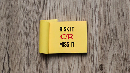 Risk it or Miss it motivational quote on yellow sticky note on rustic wooden background