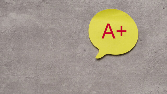 Yellow Speech Bubble with Red A Plus Grade Symbol on Textured Grey Background and Copy Space