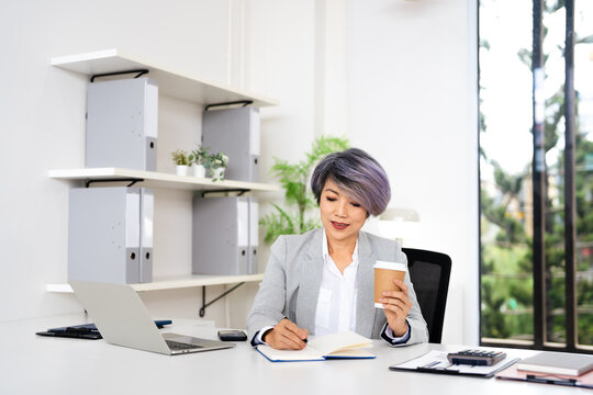 Confident mature woman, writer  using laptop computer, taking notes, working project in modern office.  financier working at workplace. Successful business - Powered by Adobe
