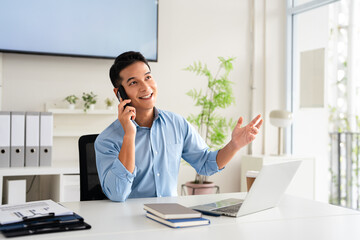 Entrepreneur making a phone call while working on a laptop. Young business man making plans and discussing a new project with a client in an office.